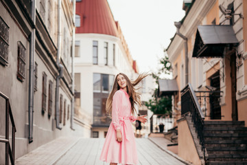 Obraz premium A young, beautiful girl in a pink dress walks through the beautiful streets in the city. Very beautiful portraits of a girl in the city.