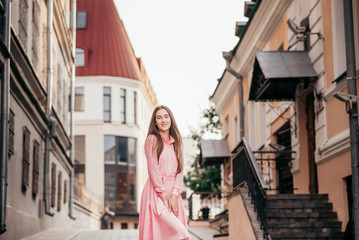 A young, beautiful girl in a pink dress walks through the beautiful streets in the city. Very beautiful portraits of a girl in the city.