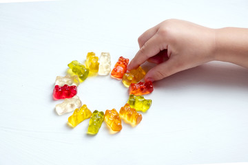 Children's vitamins in the form of bears are arranged in rows.  A lot of multi-colored jelly sweets for children.  The hand of the child reaches and takes a vitamin or candy