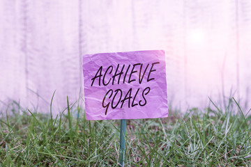 Conceptual hand writing showing Achieve Goals. Concept meaning Results oriented Reach Target Effective Planning Succeed Plain paper attached to stick and placed in the grassy land