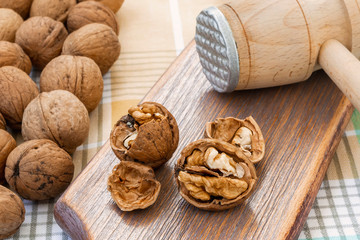 Whole and cracked walnuts (Juglans regia) near wooden meat mallet on a brown wooden board. Natural unbleached nuts. Vegetarian.