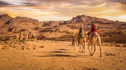 Tourists riding camels towards the Temenos Gate on the Colonnaded Street, Petra, Jordan.