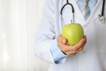 Doctor with apple and stethoscope, close up and space for text