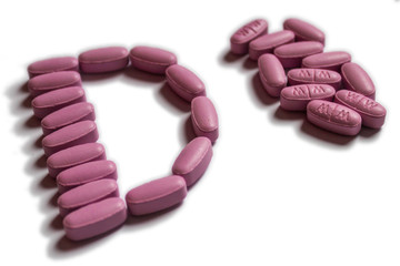 Pink oval tablets in a shape of letter D next to pile of same pills. Isolated on white background. 