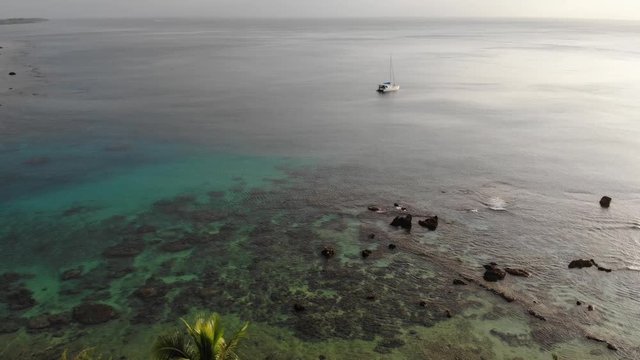 Aerial view of a catamaran yacht anchored in clear water off a tropical island with coral reef and palm trees in Vanuatu
