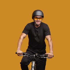 Fototapeta na wymiar Young man in black clothes and a bicycle helmet and glasses posing while sitting on a bicycle.