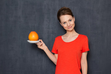 Portrait of happy young woman holding saucer with grapefruit