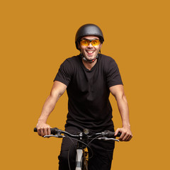 Fototapeta na wymiar Young man in black clothes and a bicycle helmet and glasses posing while sitting on a bicycle.