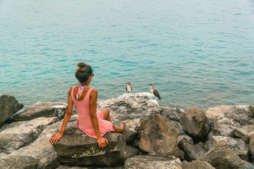 Fototapeta na wymiar Woman sitting and watching two beautiful blue footed boobie birds. Natural wildlife shot in San Cristobal, Galapagos. Boobies bird on rocks with ocean sea background. Wild animal in nature. Holiday