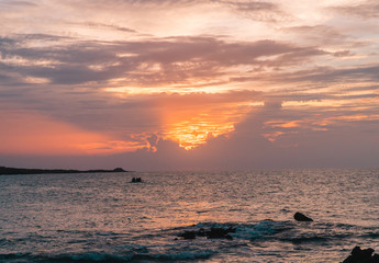 Orange sunset over ocean sea. Dramatic view of the sun setting over the sea, at sunset. View of the ocean, beach, sand and rocks. Red, pink, orange, blue sky with clouds. Shot on Galapagos Islands, Ec