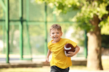 Obraz premium Running little boy with rugby ball in park