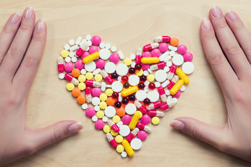hands are on the table next to pills laid out in the shape of a heart