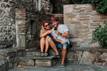 Fototapeta na wymiar Young couple using smartphone on the stairs of an old town in Greece