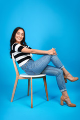 Beautiful Asian woman sitting on chair against color background