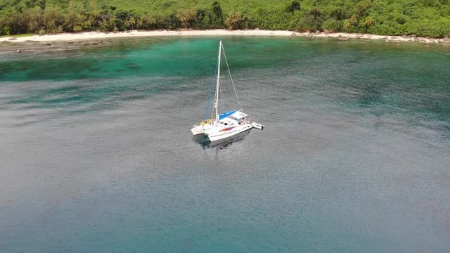 Aerial view of a catamaran yacht anchored in clear blue water and white sand off a tropical island with coral reef and palm trees in Vanuatu