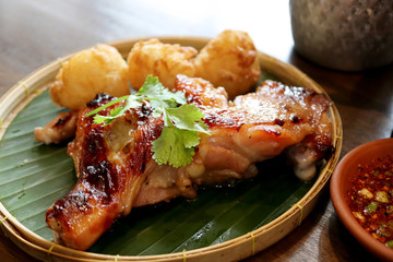 Close up Traditional Thai Grilled Chicken with fried sticky rice mix egg on threshing basket with banana leaf on wooden table background and spicy thai sauce style. Thai Foods concept.