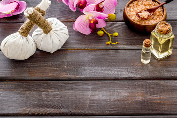 Massage thai herbal balls near spa accessories and orchids on dark wooden background copy space