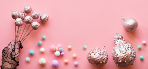 Creative pink paper flat lay, banner composition. Flat layout with glittering metallic decorative pumpkins, soft balls in pastel colors and hand in black mesh glove holding decorative fruits