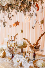 New Year mood, Christmas tree. Rectangular table covered with a gold tablecloth, decorated with candles with flowers for celebration. Festive still life by candlelight.