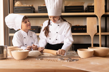Little bakers rolling dough on table