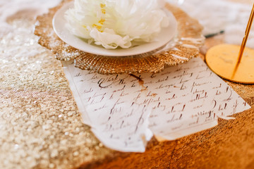 New Year mood. Table with a gold tablecloth, decorated with candles for celebration. Festive still life by candlelight. Graphics of beautiful calligraphy with a flower on a plate.