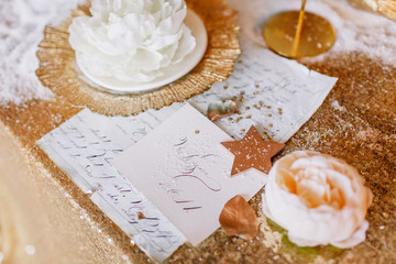 New Year mood. Table with a gold tablecloth, decorated with candles for celebration. Festive still life by candlelight. Graphics of beautiful calligraphy with a flower on a plate.