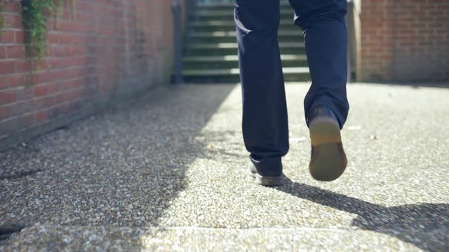 Low angle shot of Young man walking outside in city park during the day. Focused only on the feet and shoes with shallow depth of field 