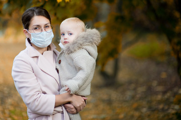 mom in a medical face mask holds a little daughter in her arms. Woman and child in medical masks.