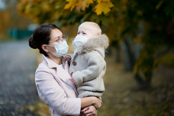 mom in a medical face mask holds a crying daughter in her arms and looks at her