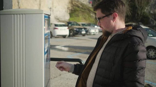 young man in glasses pays parking at meter