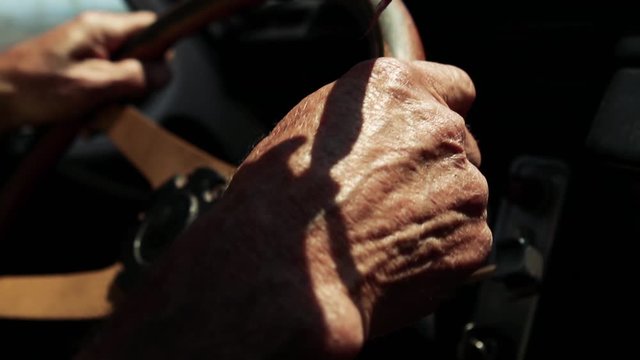 Wrinkled Hands of a Senior Man driving an Old Car. Close-Up.