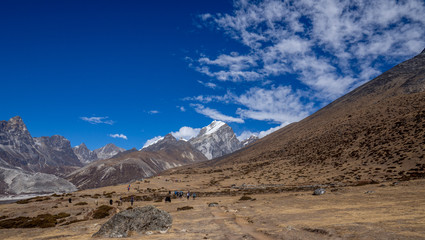 Fototapeta na wymiar Trekkers walking through an open plain with the peaks of the Himalayas in Nepal during the Everest Base Camp trek