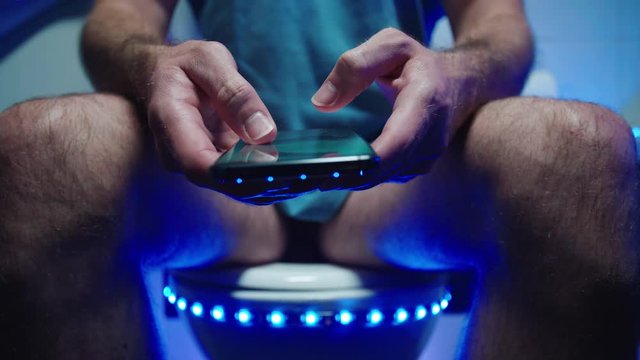 Person on toilet checking the social networks on smartphone 4K. Low angle close up on the smartphone in focus while person taking a shit.