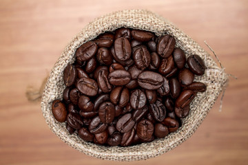 Close up, brown coffee beans in a cloth bag on an old wooden background. Top view.