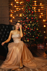 Elegant lady in luxury dress over christmas tree lights background. Happy New Year. Merry Christmas. Beautiful smiling woman. Healthy long hair. People, holidays and magic concept