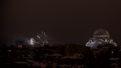 Panning shot of fireworks in the sky next to an impressive orthodox christian church on the top of a city scape.