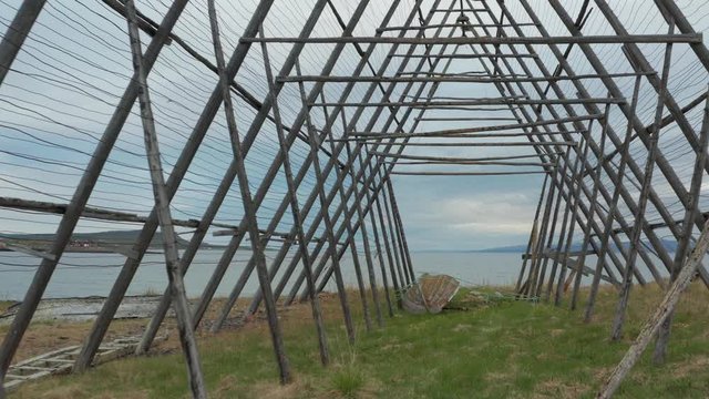 Aerial video with Drone flying through an old fish flake with sea view and an old boat visible on the ground