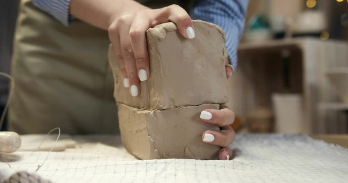 Close up of the hands of the young Caucasian woman artist sharing a big piece of the clay in two parts and start molding it.