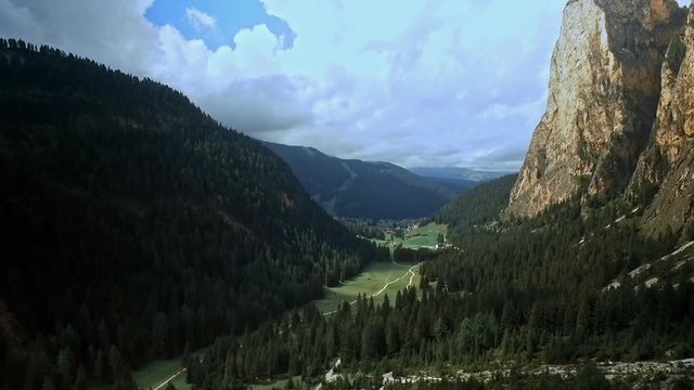 Sideways flight left to right across a beautiful alpine mountain valley with sheer rock on the right and wooded hills on the left.