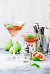 Pink fig martini alcoholic cocktail in shot glass on gray table with bar tools, copy space