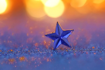 Christmas and New Year background.Winter holidays wallpaper.Blue star macro on a blue glitter background with orange bokeh.Festive  shiny background