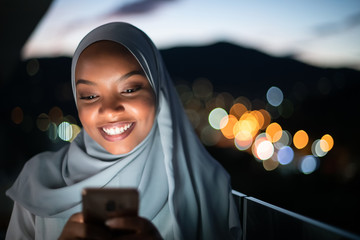 Young Muslim woman on  street at night using phone