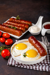 Breakfast - Fried eggs and meat sausages and sauces against a dark background. Selective focus. Copy space