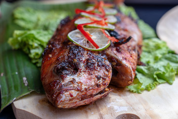 Fried fish with fresh green salad and lemon of Bali, Indonesia, closeup. Delicious roasted sea fish with lemon on wooden plate in restaurant