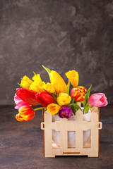 Bouquet of tulips and narcissuses in a basket. Spring flower background. Selective focus. Copy space