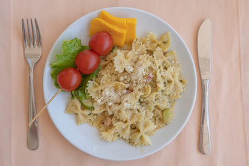 Pasta farfalle with cherry tomato and cheese in white plate, closeup