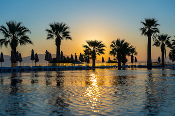Fototapeta na wymiar Magical sunrise with silhouette coconut palm tree and swimming pool in luxury hotel resort near sea. Beautiful morning seascape