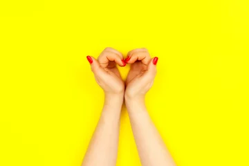 Poster Nails design. Two beautiful woman's hands with red manicure look like heart on yellow background. Place for text. © Konstantin