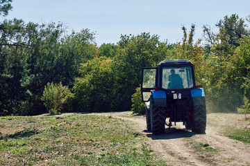 Fototapeta premium a blue tractor with big wheels rides on a dusty dirt road in the middle of the forest on a hot summer day