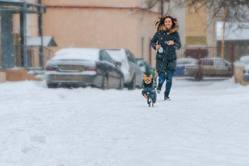 girl running with a chihuahua in warm clothes on a frosty winter day over fresh white snow